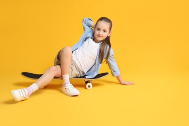 Stylish girl sitting on skateboard against yellow background, space for text