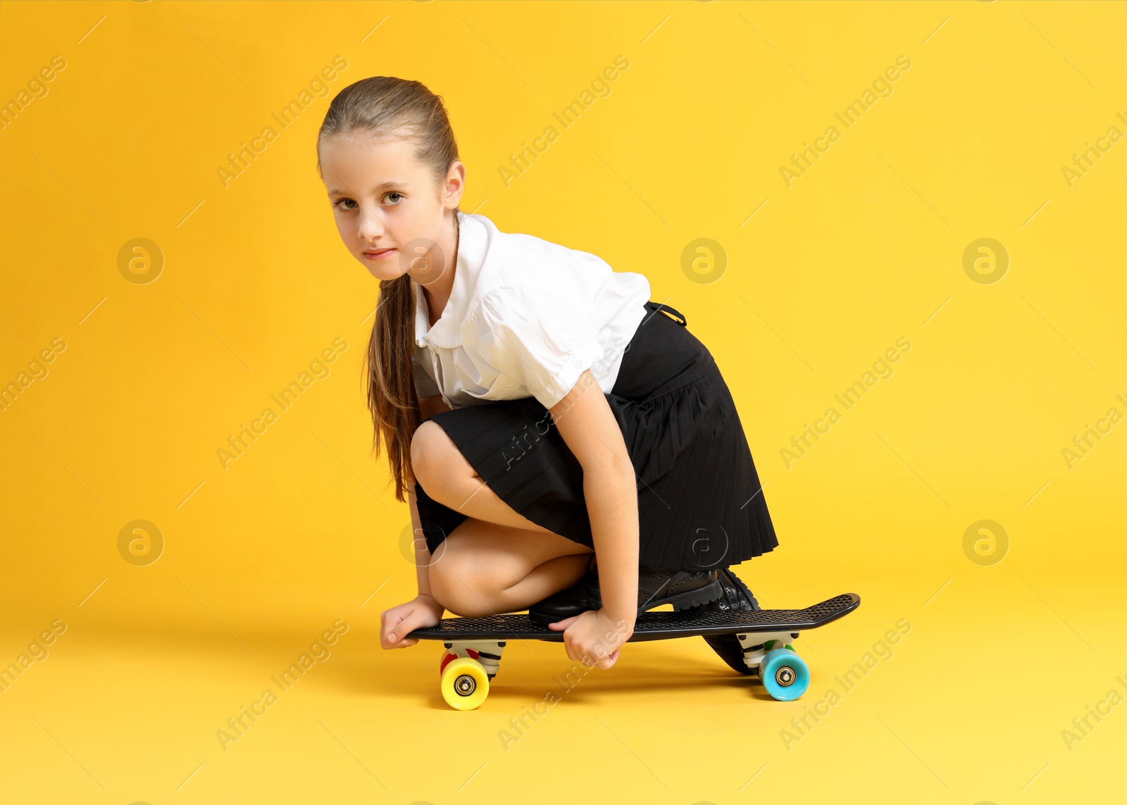 Photo of Little girl with penny board on yellow background