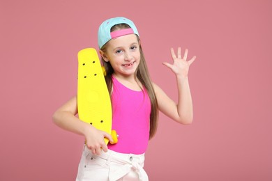 Little girl with penny board on pink background