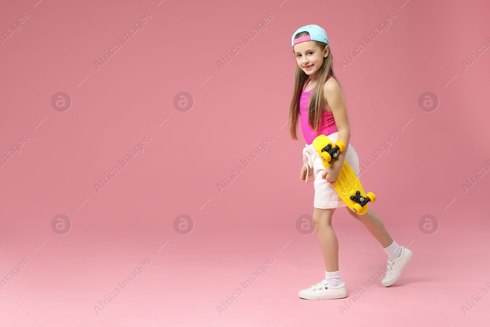 Photo of Little girl with penny board on pink background, space for text