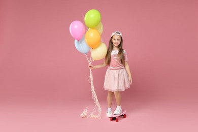 Little girl with colorful balloons and penny board on pink background