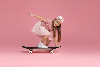 Little girl with skateboard against pink background