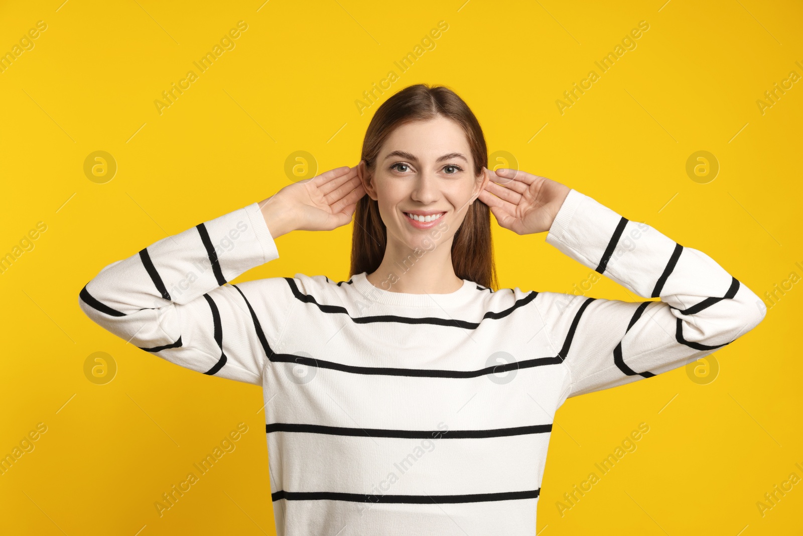 Photo of Woman showing hand to ear gesture on dark yellow background