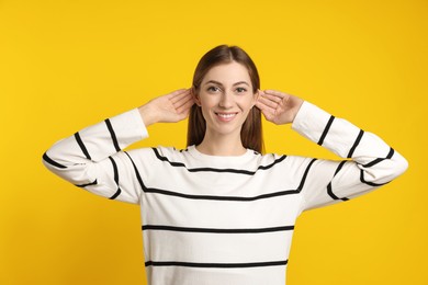 Photo of Woman showing hand to ear gesture on dark yellow background