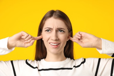 Photo of Woman covering her ears with fingers on dark yellow background