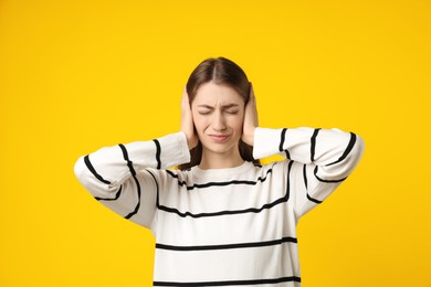 Photo of Woman covering her ears on dark yellow background