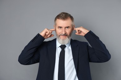 Photo of Senior man covering his ears with fingers on grey background