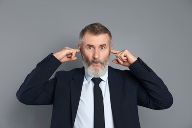 Photo of Senior man covering his ears with fingers on grey background