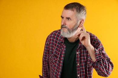 Photo of Senior man showing hand to ear gesture on orange background, space for text