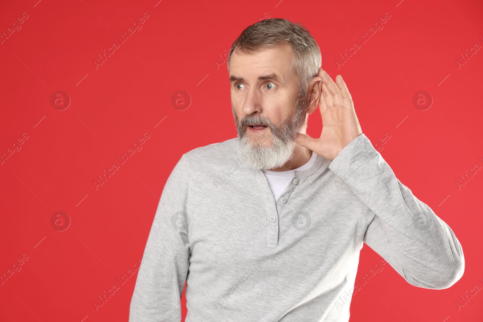 Photo of Senior man showing hand to ear gesture on red background