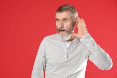 Photo of Senior man showing hand to ear gesture on red background