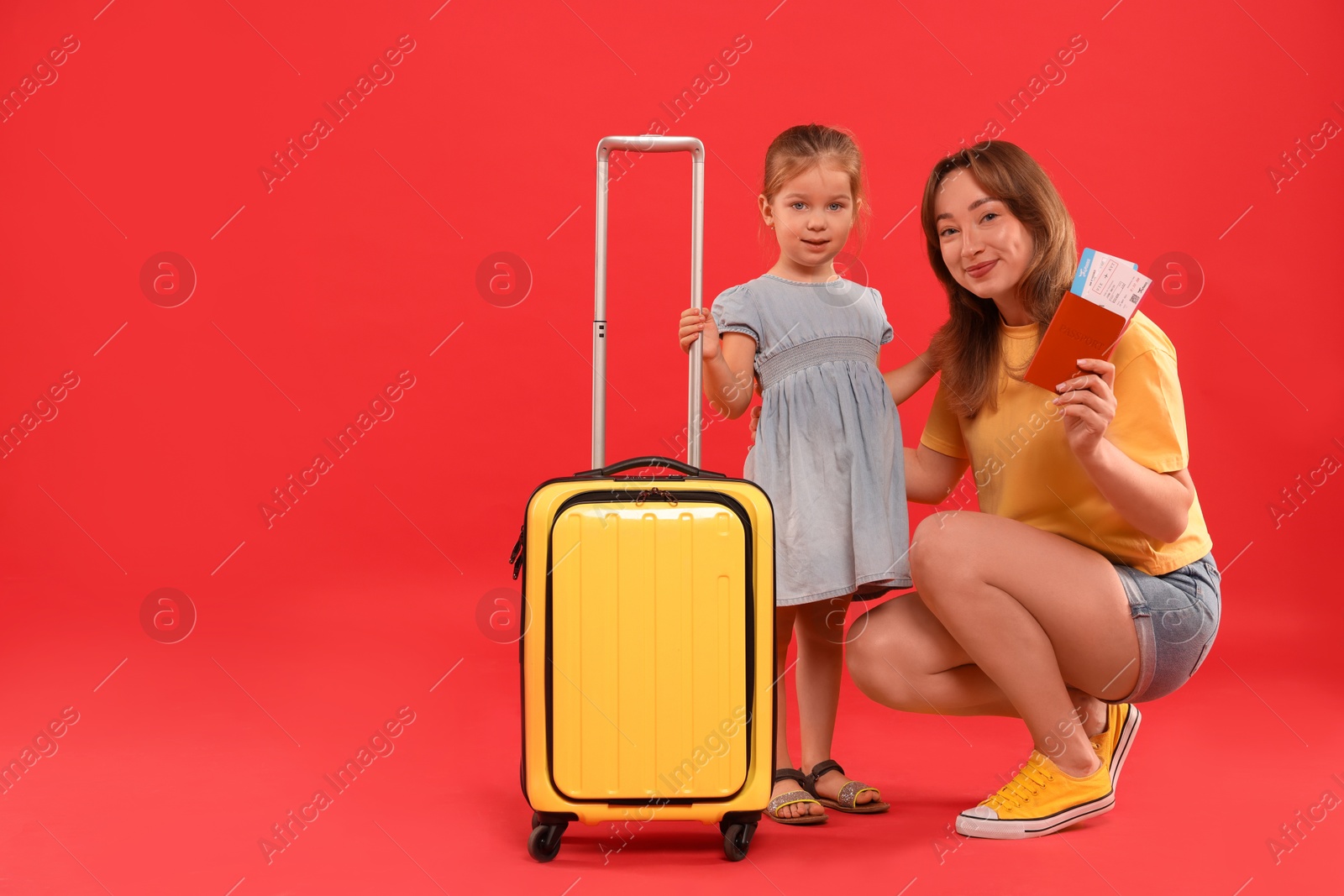 Photo of Traveller with suitcase. Young woman and cute little girl on red background, space for text