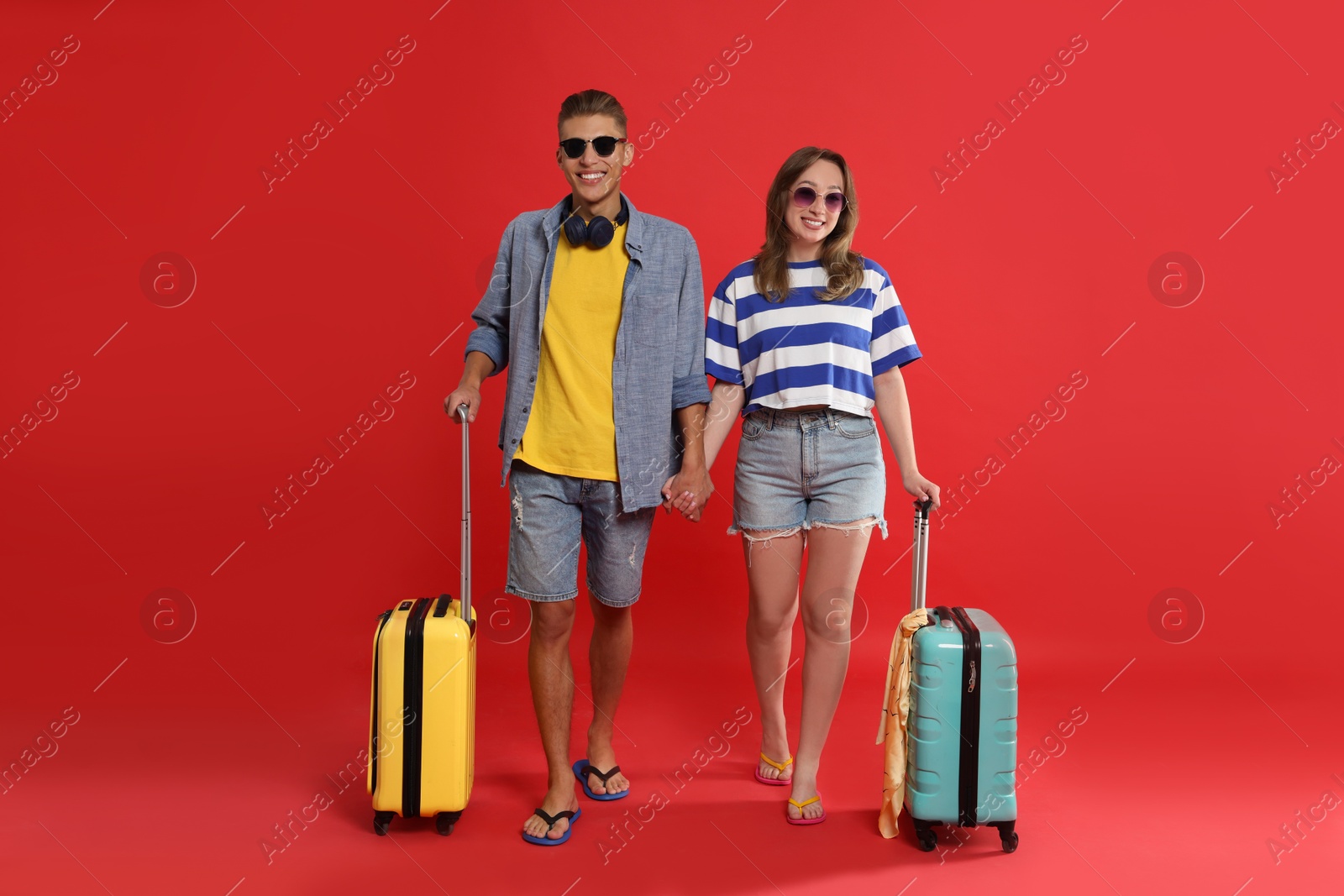 Photo of Happy travellers with suitcases on red background