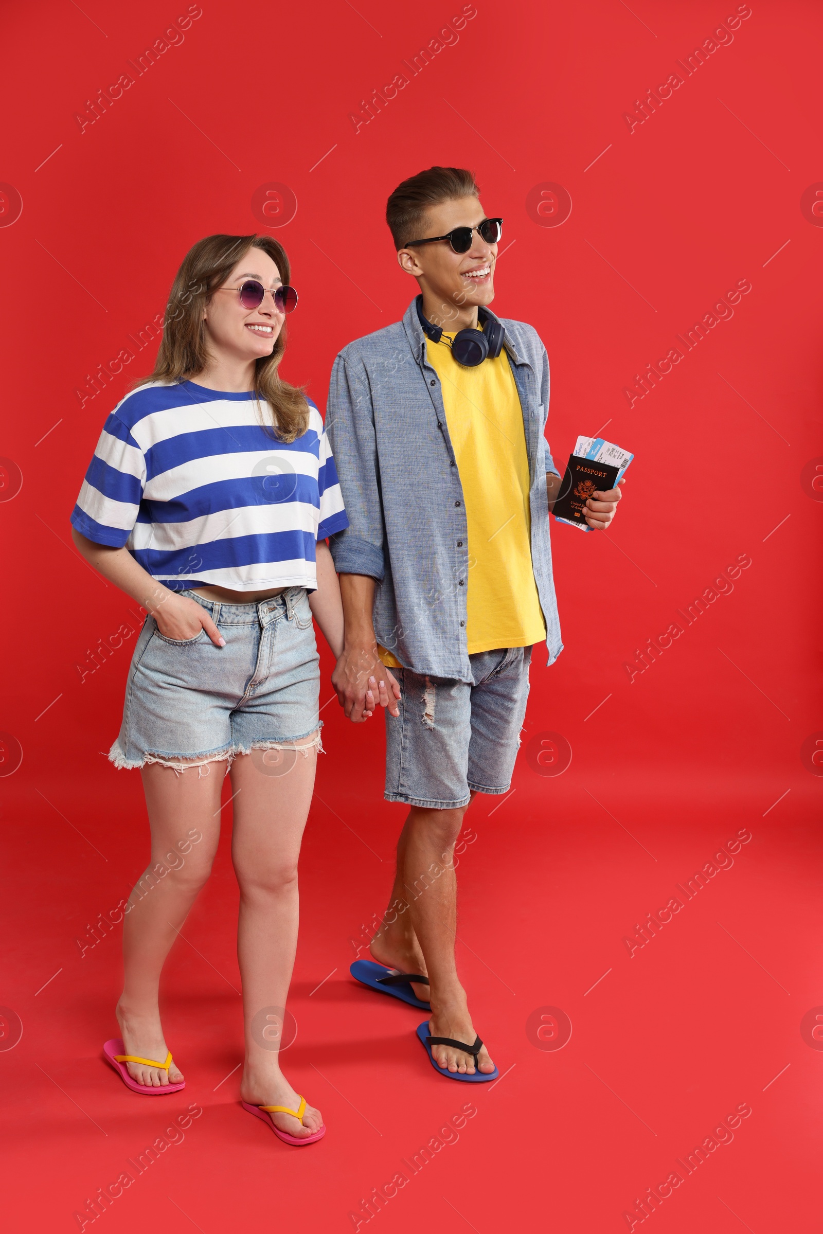 Photo of Travellers with passport and tickets. Happy young woman and man holding hands on red background