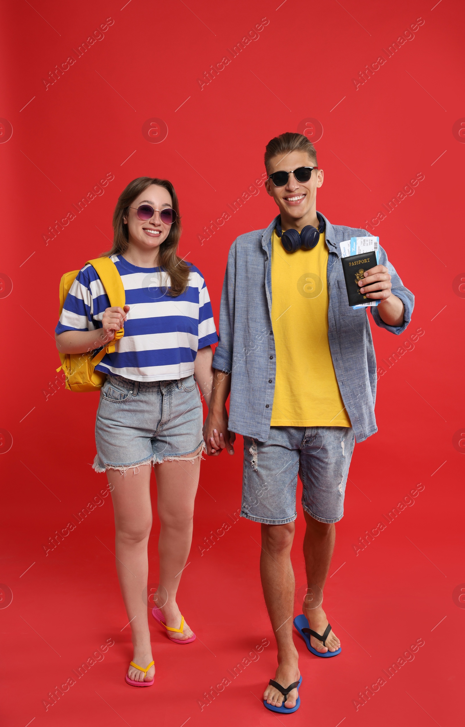 Photo of Travellers with passport and tickets. Happy young woman and man holding hands on red background