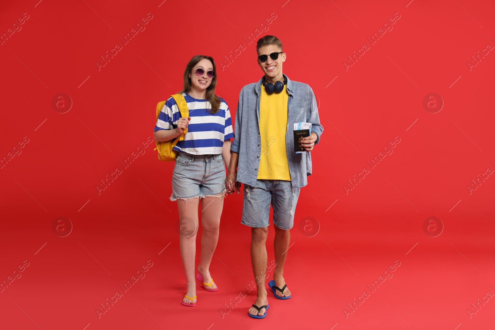 Photo of Travellers with passport and tickets. Happy young woman and man holding hands on red background