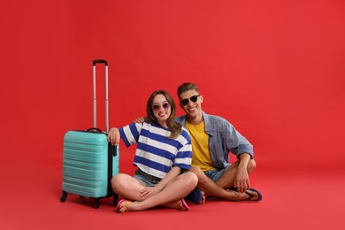 Photo of Happy travellers with suitcase on red background