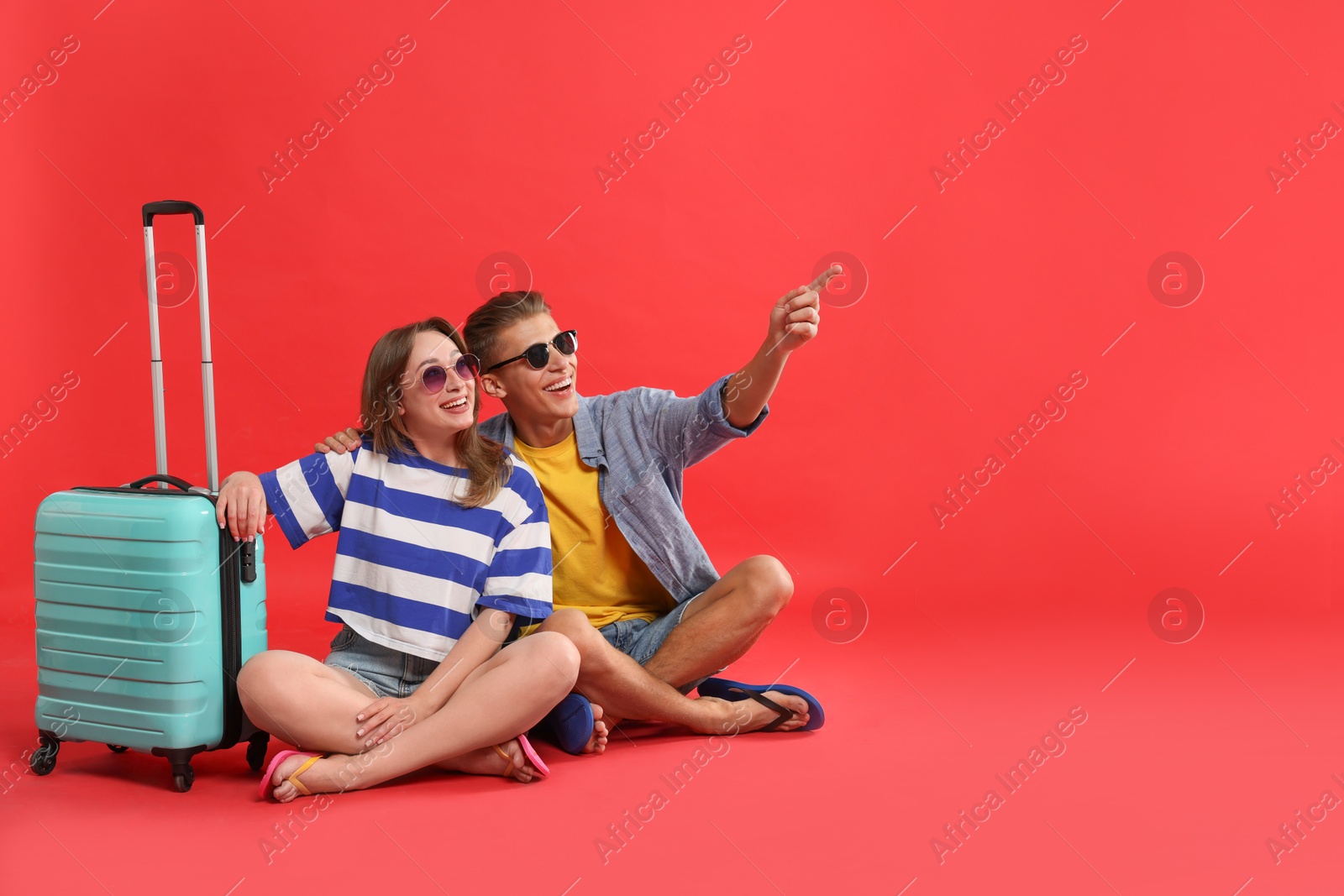 Photo of Happy travellers with suitcase looking at something on red background. Space for text