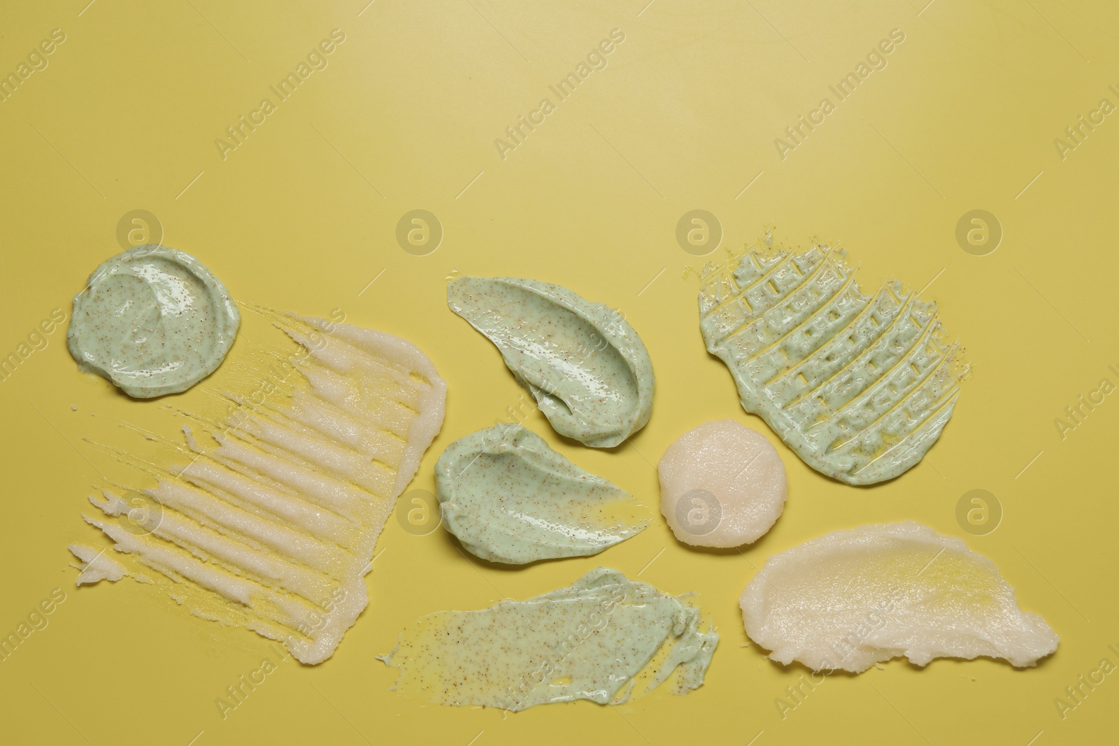 Photo of Samples of different body scrubs on yellow background, top view