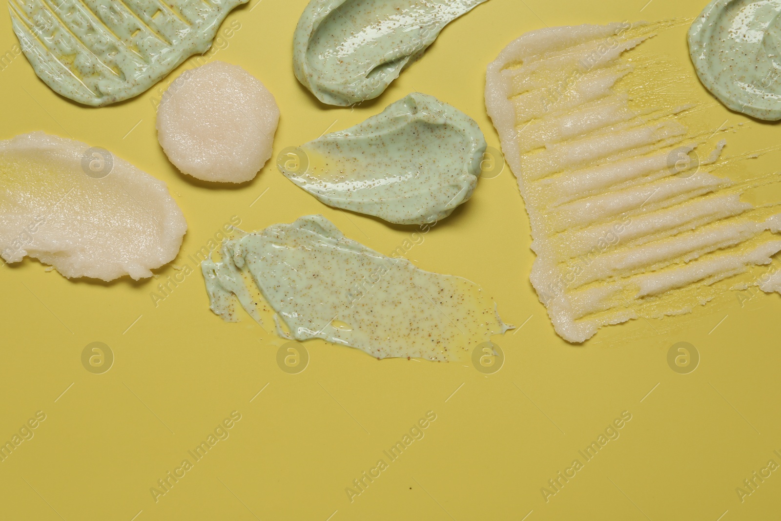 Photo of Samples of different body scrubs on yellow background, top view