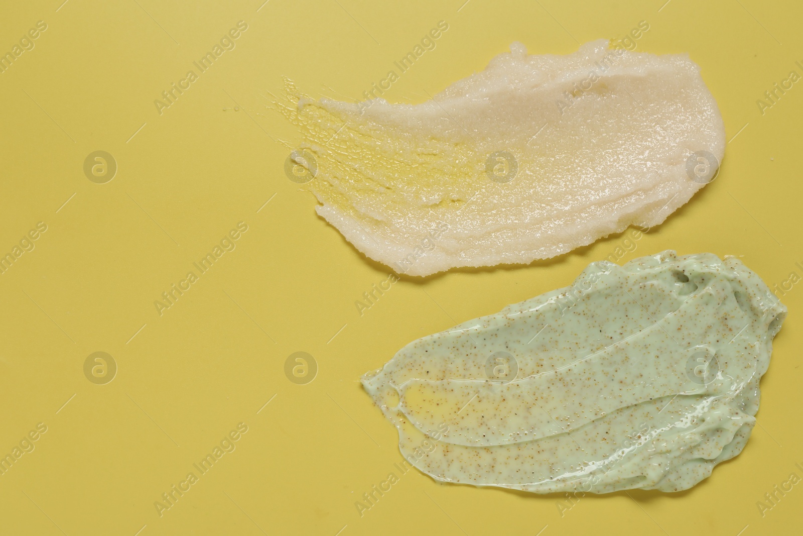 Photo of Samples of different body scrubs on yellow background, top view. Space for text