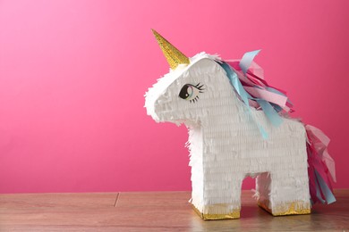 Photo of Beautiful pinata in shape of unicorn on wooden table against pink background. Space for text