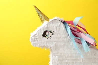 Photo of Beautiful pinata in shape of unicorn on yellow background, closeup. Space for text