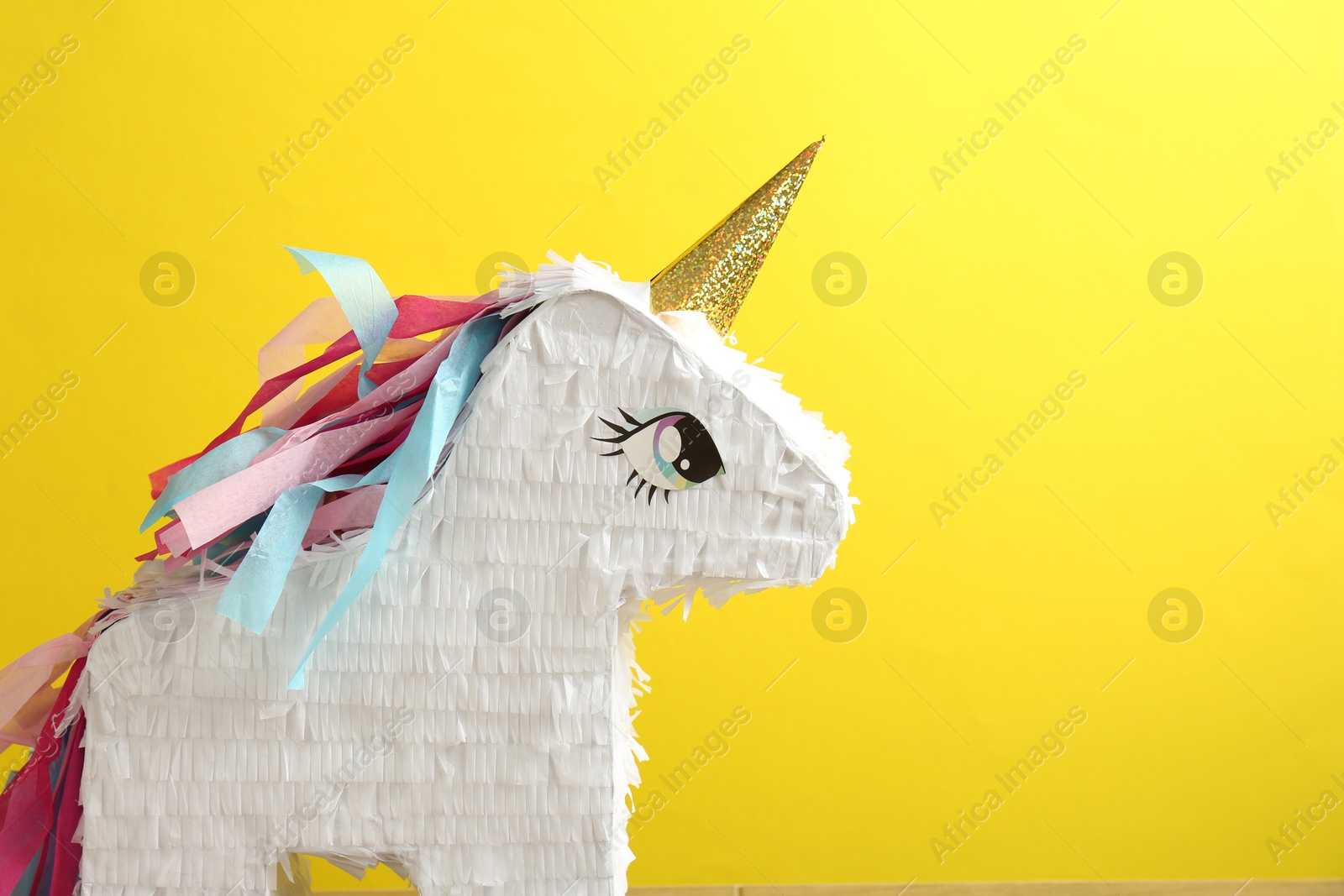 Photo of Beautiful pinata in shape of unicorn on yellow background, closeup. Space for text