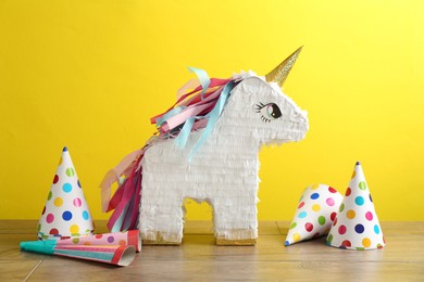 Photo of Beautiful pinata in shape of unicorn, party cones and poppers on wooden table against yellow background