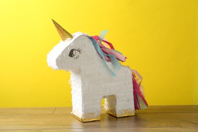 Photo of Beautiful pinata in shape of unicorn on wooden table against yellow background