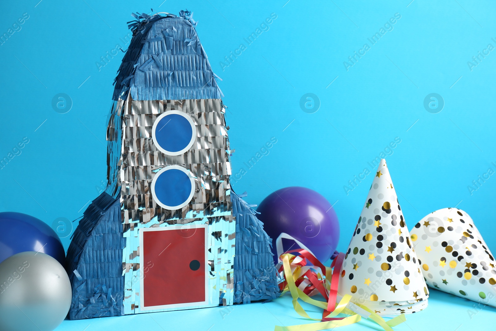 Photo of Beautiful pinata in shape of rocket, party cones and balloons on blue background