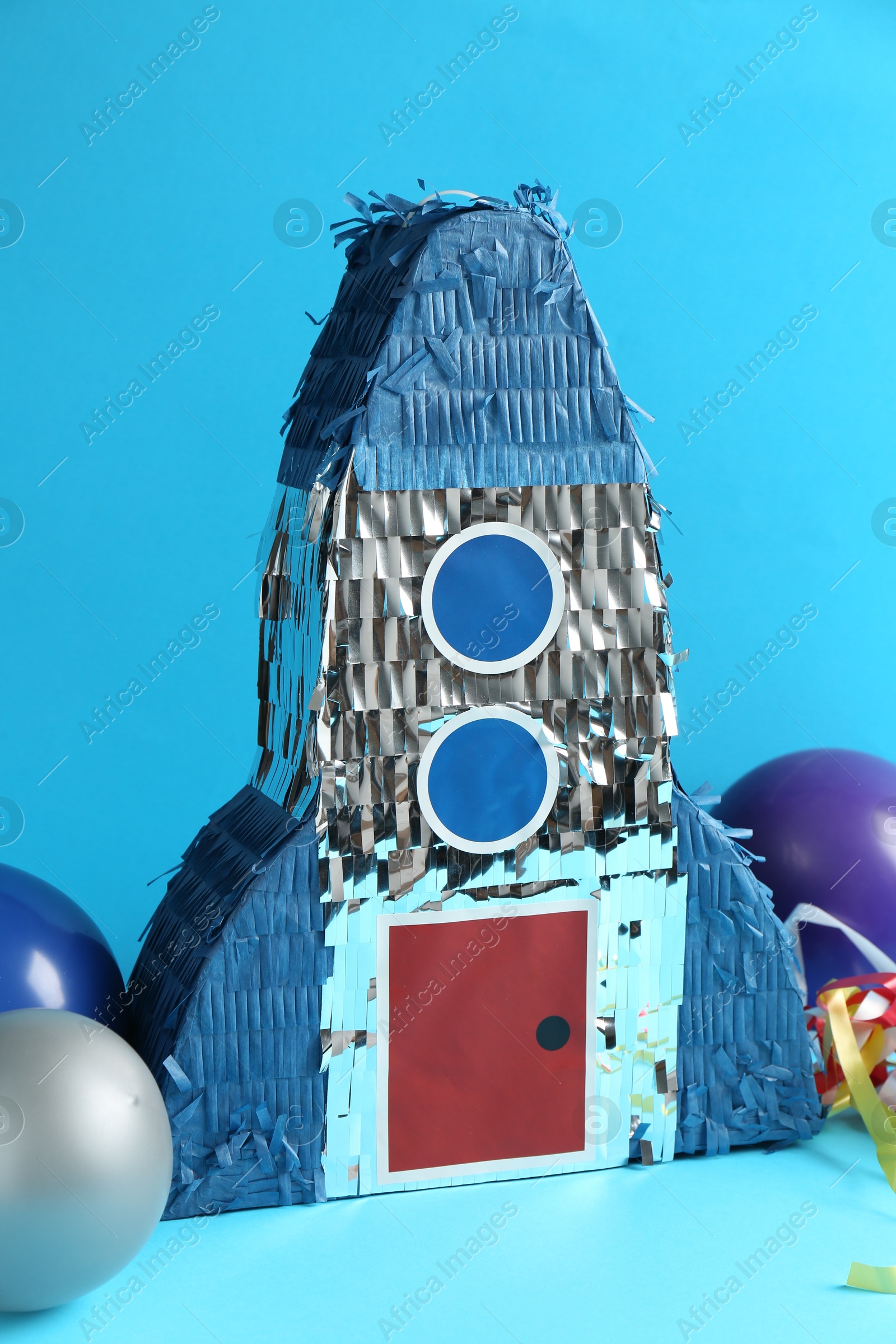 Photo of Beautiful pinata in shape of rocket and balloons on blue background