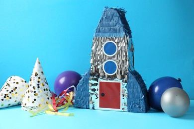 Photo of Beautiful pinata in shape of rocket, party cones and balloons on blue background