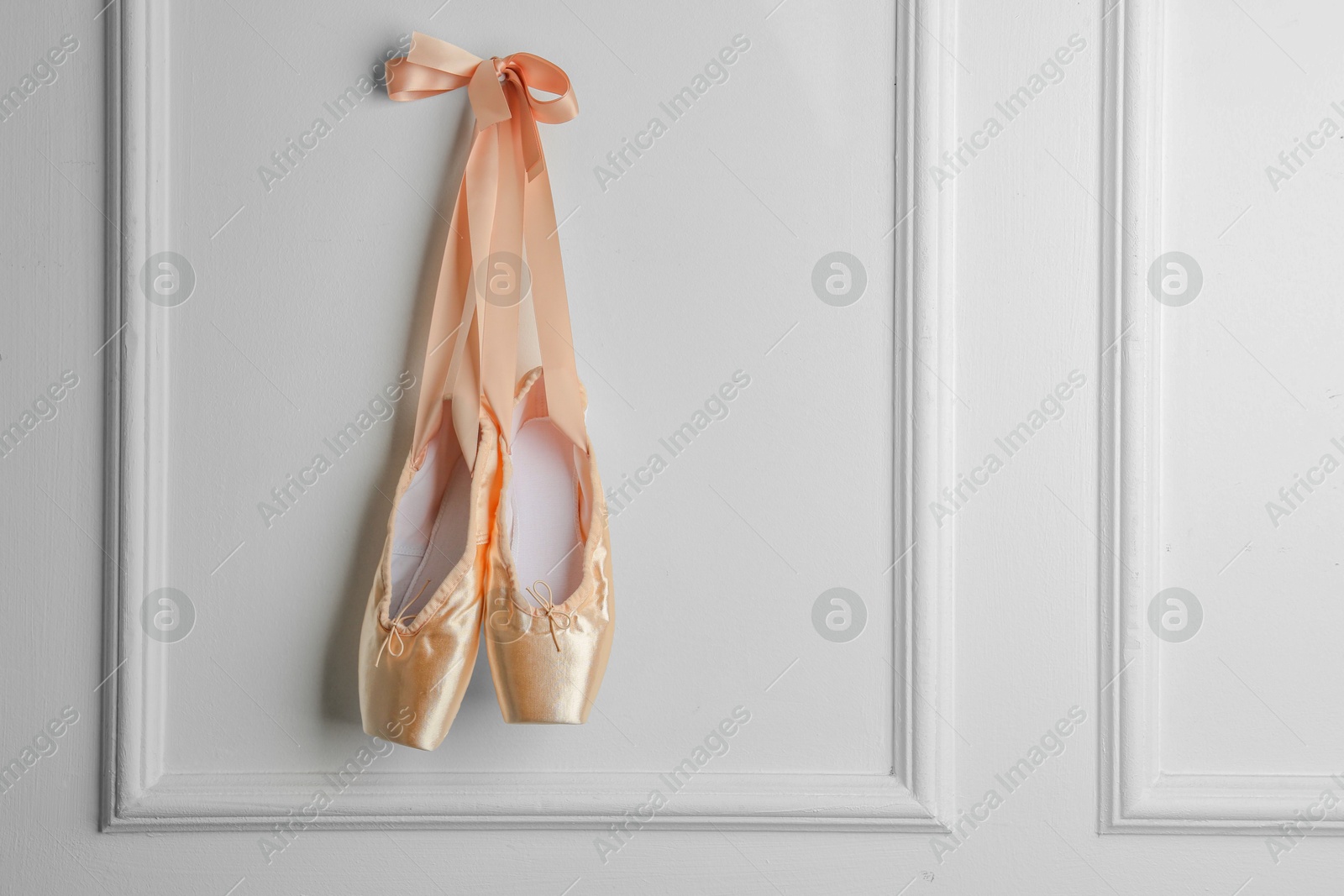 Photo of Pair of beautiful pointe shoes hanging on white wall, space for text