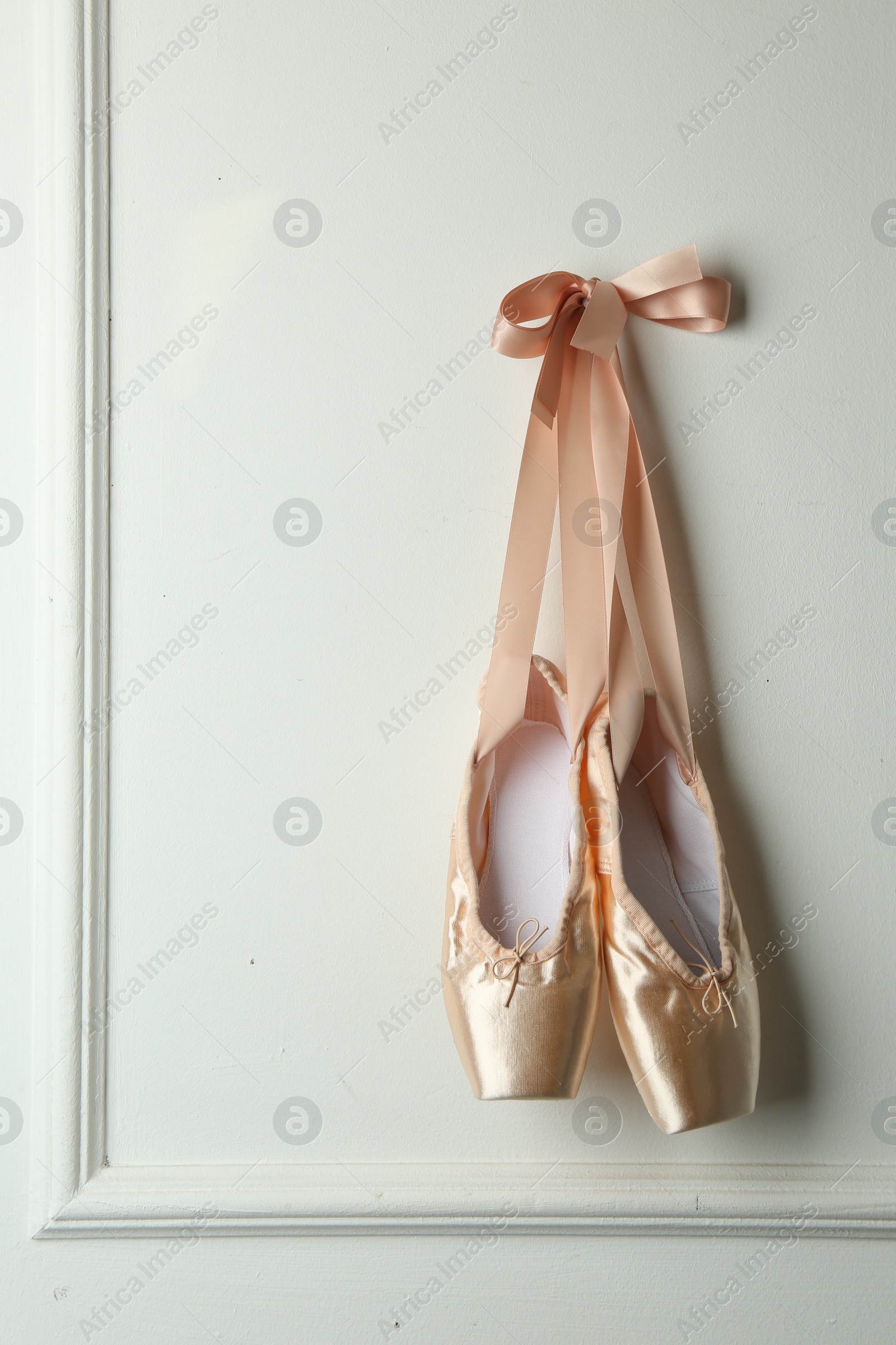 Photo of Pair of beautiful pointe shoes hanging on white wall. Space for text