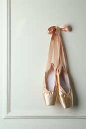 Photo of Pair of beautiful pointe shoes hanging on white wall. Space for text