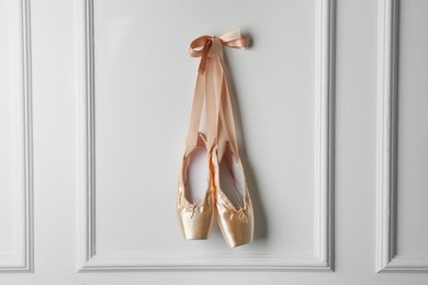 Photo of Pair of beautiful pointe shoes hanging on white wall