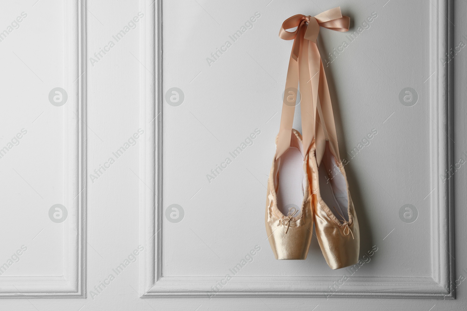 Photo of Pair of beautiful pointe shoes hanging on white wall, space for text