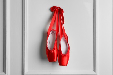 Photo of Pair of beautiful red pointe shoes hanging on white wall