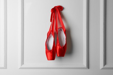 Photo of Pair of beautiful red pointe shoes hanging on white wall