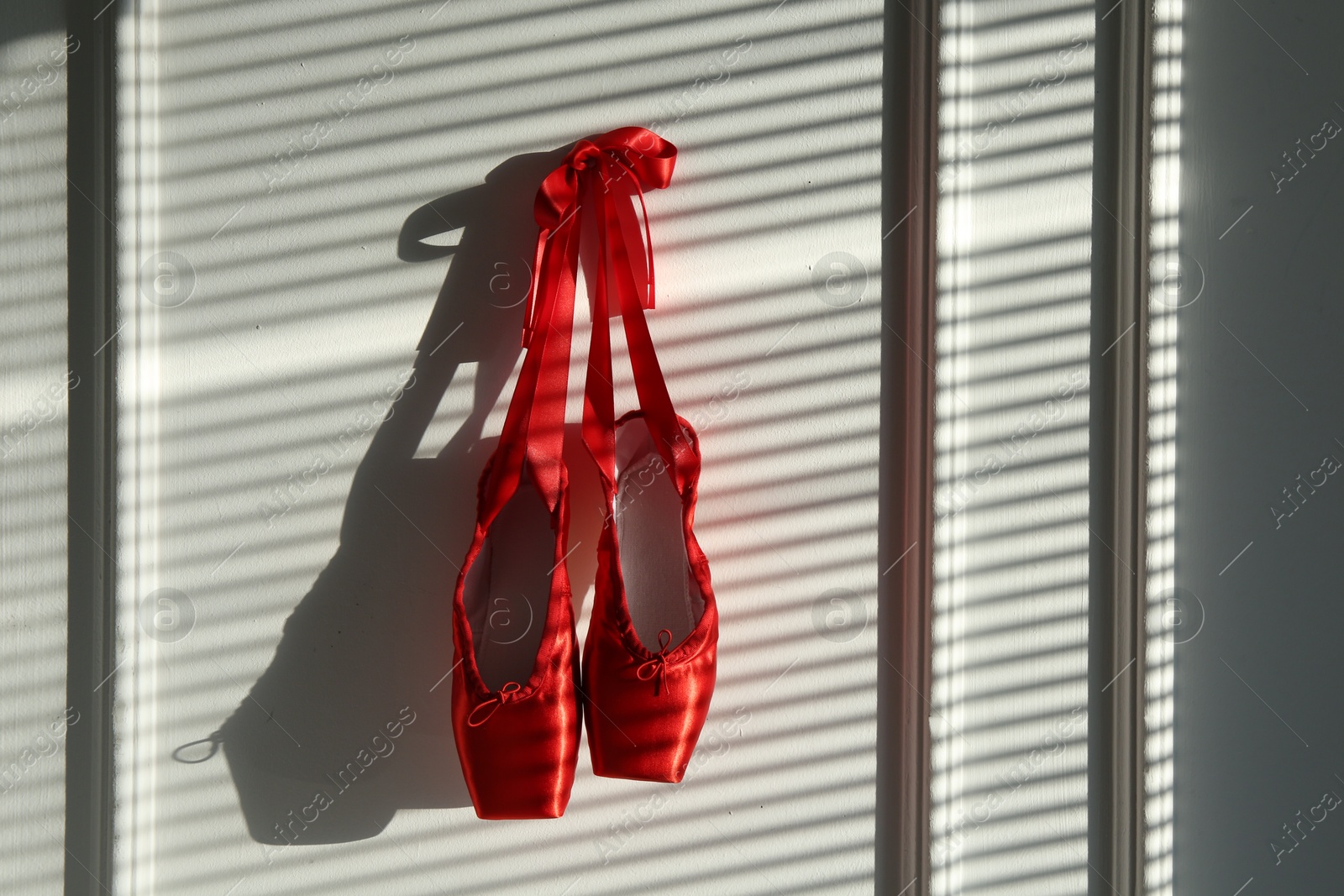 Photo of Pair of beautiful red pointe shoes hanging on white wall