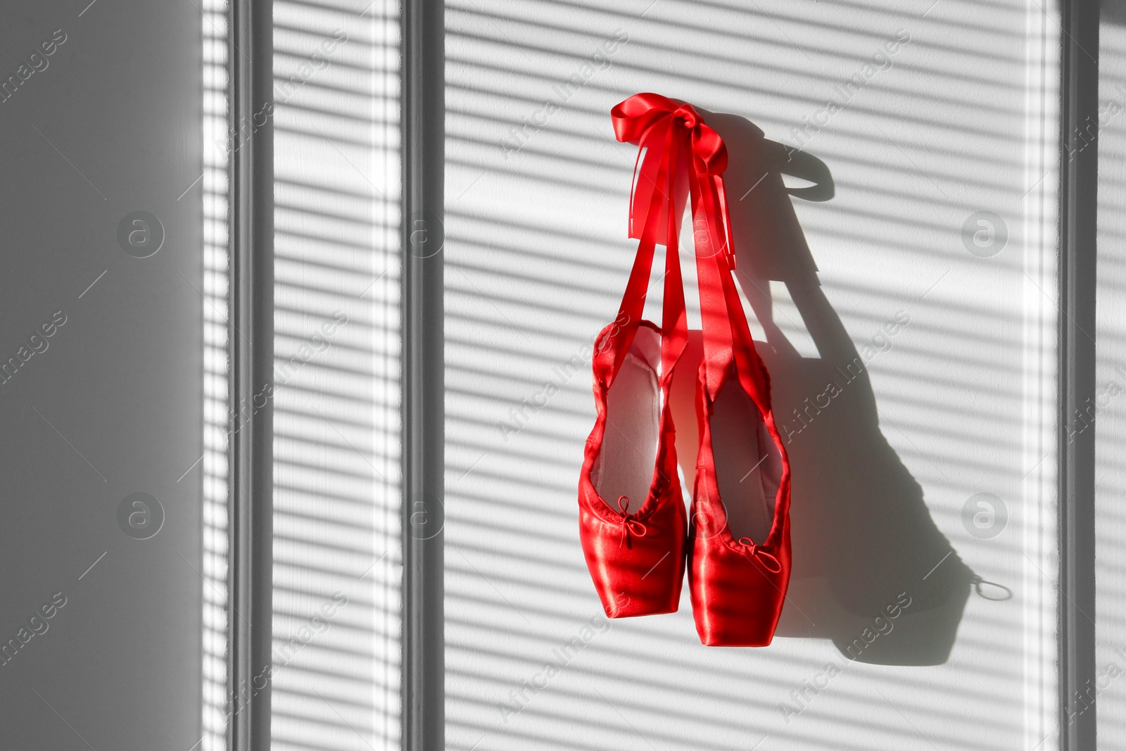 Photo of Pair of beautiful red pointe shoes hanging on white wall, space for text