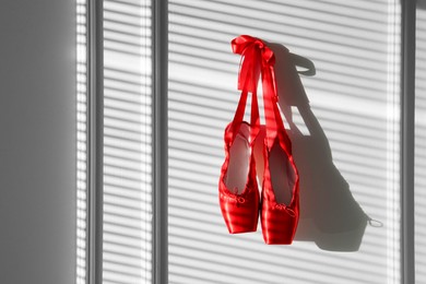 Photo of Pair of beautiful red pointe shoes hanging on white wall, space for text