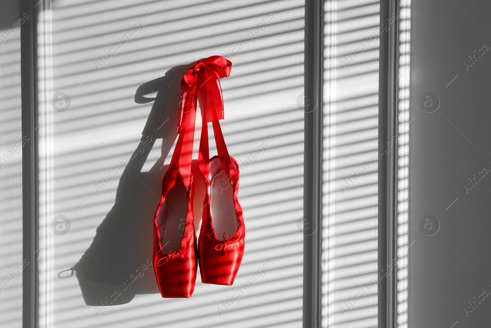 Photo of Pair of beautiful red pointe shoes hanging on white wall, space for text