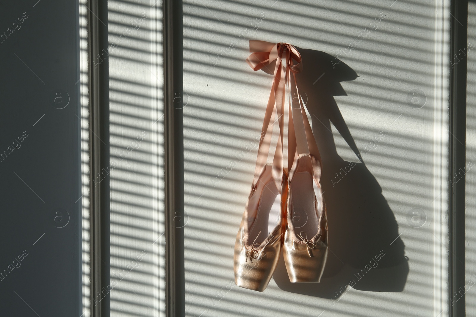 Photo of Pair of beautiful pointe shoes hanging on white wall