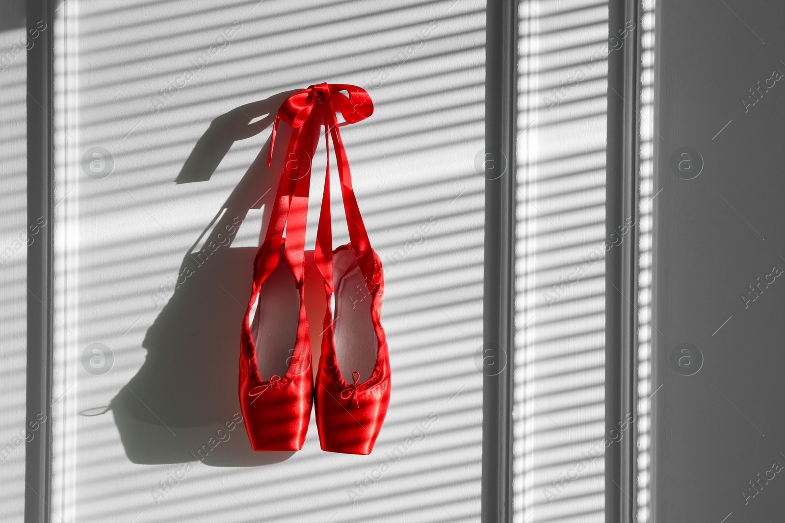 Photo of Pair of beautiful red pointe shoes hanging on white wall, space for text