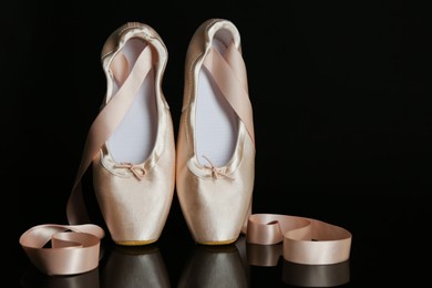 Photo of Pair of beautiful pointe shoes on black mirror surface