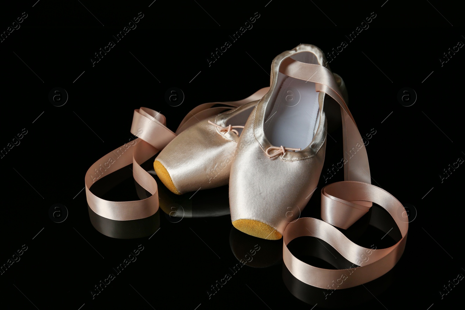 Photo of Pair of beautiful pointe shoes on black mirror surface