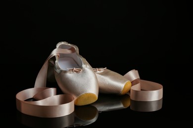 Photo of Pair of beautiful pointe shoes on black mirror surface