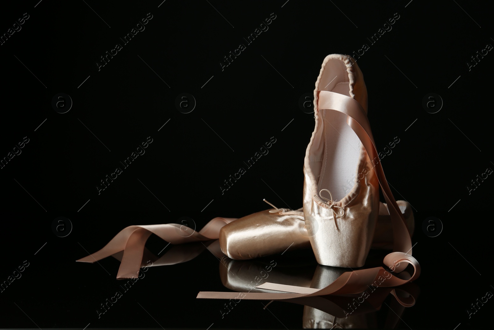 Photo of Pair of beautiful pointe shoes on black mirror surface, space for text